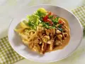 Ein Teller mit geschnetzeltem Fleisch mit Pilzen in cremiger Sauce, dazu Spätzle, Salat und Zitronenspalten.