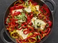 Gebackener Feta mit bunten Paprikastreifen, Kapern und frischen Kräutern in einer gusseisernen Pfanne.