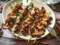 Gegrillte Champignons auf Spießen, mit Kräutern verfeinert und auf einem Teller mit Dip serviert. Ein Genuss für jeden Pilzliebhaber!