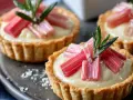 Drei kleine Rhabarber Tartelettes mit cremiger Füllung und frischen Rhabarberstücken, garniert mit Rosmarin.