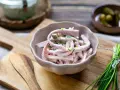 Schmackhaftes Fleischsalat-Rezept mit Gurkenstückchen und Schnittlauch garniert, serviert in einer Schale auf einem Holzbrett.
