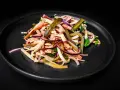 Ein appetitlicher Schweizer Wurstsalat mit Wurststreifen, Käse, roten Zwiebeln und Gewürzgurken auf einem dunklen Teller.