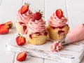 Erdbeer Cupcakes mit rosa Frosting und frischen Erdbeeren. Ein Spritzbeutel zeigt, wie die leckeren Erdbeer Cupcakes entstehen.