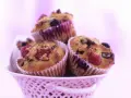 Saftige Muffins mit Obst und Joghurt, garniert mit frischen Himbeeren und Blaubeeren, in einem rosa Körbchen.