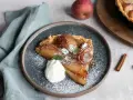 Ein Stück Quitten Tarte Tatin, bestäubt mit Puderzucker und garniert mit Sahne und Minze.