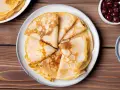 Omas Pfannkuchen-Rezept: goldbraune, gefaltete Pfannkuchen auf einem Teller, daneben eine Schüssel mit Kirschen.