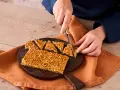 Ein Nussecken Rezept wird hier gezeigt. Eine Person schneidet die süßen Nussecken auf einem Holzbrett.