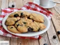 Saftige Blaubeer Cookies auf einem Teller, daneben frische Blaubeeren und eine rot-weiße karierte Serviette.
