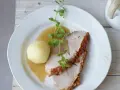 Ein knuspriger Schweinebraten mit Soße und Klößen, perfekt für ein deftiges Schweinebraten Rezept. Frisch garniert mit Kräutern.
