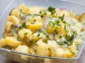 Ein köstlicher Kartoffelsalat ohne Mayo, mit Gurkenstücken und frischem Schnittlauch garniert, in einer Glasschüssel.