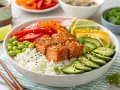 Eine bunte Lachs Bowl mit Reis, Edamame, Gurken, Paprika, Karotten und Limette.