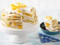 Eine köstliche Pfannkuchen Torte mit Pfirsichen und Sahne, auf einem weißen Tortenständer und ein Stück in einer kleinen Pfanne.