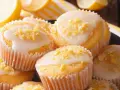 Leckere zitronenmuffins rezept: goldgelbe Muffins mit weißer Glasur und Zitronenschale bestreut, daneben frische Zitronenscheiben.