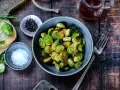 Gerösteter Rosenkohl in einer Schüssel, bereit für leckere Rezepte mit Rosenkohl. Daneben Salz, Pfeffer und ein Glas Sirup.