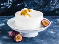 Eine weiße Maracuja Torte mit frischer Maracuja-Frucht und Sahnetupfern, umgeben von ganzen und halbierten Maracujas.