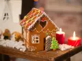 Ein zauberhaftes Lebkuchenhaus, das Lust macht, es selber zu machen. Verziert mit bunten Smarties und Zuckerguss, steht es neben Kerzen und Weihnachtsfiguren.