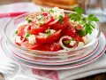 Frischer Tomaten Feta Salat mit Zwiebelringen und Petersilie, garniert mit schwarzem Pfeffer und Meersalz.