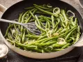 Grüne Bohnen mit Zwiebelringen in einer Pfanne, bereit zum Kochen. Daneben eine Schale mit grobem Salz.