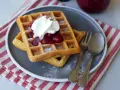 Zwei Hefewaffeln mit Trockenhefe, garniert mit Kirschkompott und Sahne, bestäubt mit Puderzucker.