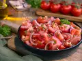 Frischer Tomatensalat mit roten Zwiebeln und Petersilie, serviert in einer schwarzen Schüssel. Das Tomatensalat Dressing ist leicht und würzig.