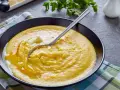 Cremige Polenta mit Butter, ein einfaches und köstliches polenta rezept, serviert in einer schwarzen Schüssel auf kariertem Tuch.