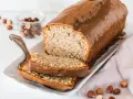Saftiger Mohn Nuss Kuchen mit Schokoladenglasur, daneben ein Glas mit Haselnüssen und zwei angeschnittene Scheiben.