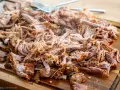 Ein Haufen zartes, **gezupftes Fleisch** liegt auf einem Holzbrett, bereit für leckere Sandwiches oder Tacos. Eine Gabel liegt daneben.