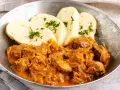 Herzhaftes Szegediner Gulasch mit Klößen, garniert mit Petersilie, serviert in einer Metallschüssel.