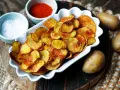 Selbstgemachte Kartoffelchips, goldbraun und knusprig, mit Salz und Paprikapulver daneben. So einfach kannst du Chips selber machen!