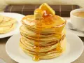 Ein Stapel goldbrauner Pancakes, übergossen mit Honig und Butter, daneben eine Tasse Kaffee. Perfekt für ein leckeres Pancakes Rezept.