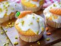 Leckere Karotten Muffins mit weißer Glasur und Marzipan-Karotten, bestreut mit gehackten Pistazien.