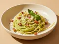 Cremige Avocado-Pasta mit knusprigem Speck, Parmesan und frischem Basilikum garniert. Ein köstliches Gericht, das Lust auf mehr macht.