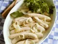 Saure Zipfel in einer Schüssel mit Zwiebelringen, Lorbeerblatt und Petersilie.