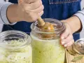 Hände pressen Kohl für ein einfaches Sauerkraut Rezept in ein Glas.