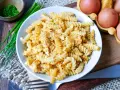 Fusilli-Nudeln mit Rührei, bestreut mit Pfeffer. Daneben liegen frische Eier und Schnittlauch. Ein einfaches Gericht: Nudeln mit Ei.