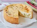 Ein saftiger Rhabarberkuchen, schnell gebacken und mit Puderzucker bestäubt. Daneben liegen frische Rhabarberstangen.
