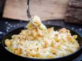 Ein Gabel hebt cremiges, überbackenes Mac n Cheese aus einer Pfanne. Dieses amerikanische Original-Rezept ist ein Genuss!