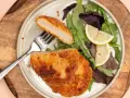 Knuspriges Kohlrabi-Schnitzel mit Salat und Zitrone auf einem Teller.