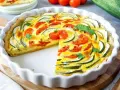 Eine köstliche Zucchini-Quiche mit Tomaten und frischer Petersilie, in einer weißen Quicheform, ein Stück fehlt.