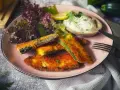 Knuspriges Zucchini-Schnitzel auf rosa Teller, serviert mit Dip, Salat und Zitrone. Ein Genuss für jeden Tag!