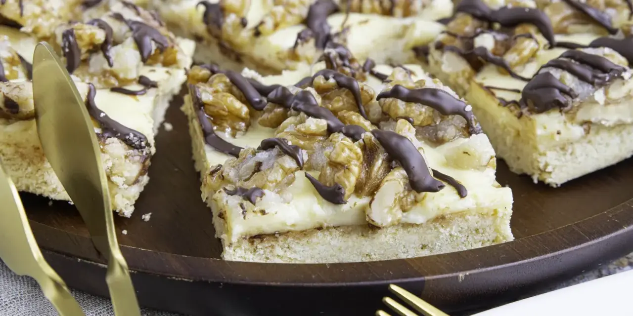 Ein "friss dich dumm kuchen" mit cremiger Füllung, Walnüssen und Schokoladendrizzle auf einem Holztablett. Goldene Gabel und Messer liegen daneben.