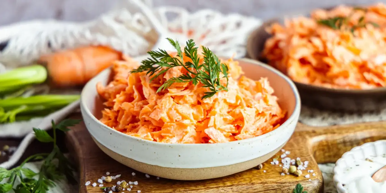 Karottensalat mit cremigem Dressing, wie im Restaurant. Frisch geriebene Karotten, garniert mit Dill, auf einem Holzbrett.