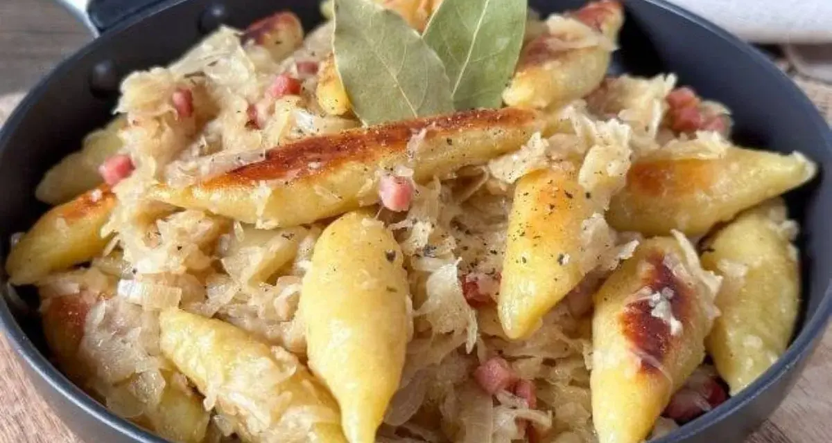 Schupfnudeln mit Sauerkraut, Speck und Lorbeerblättern in einer Pfanne. Ein herzhaftes Gericht, das zum Genießen einlädt.