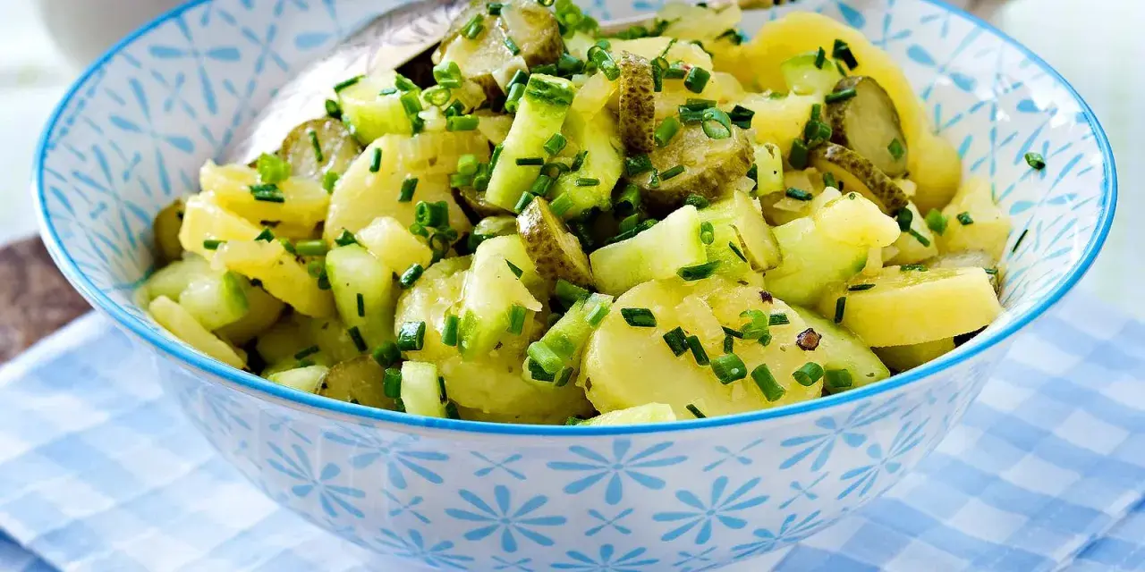Schüssel mit Kartoffelsalat mit Gurken und Schnittlauch, garniert mit frischen Kräutern.
