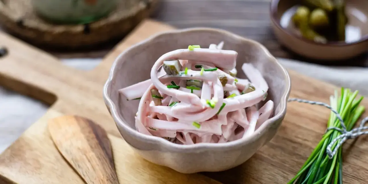 Schmackhaftes Fleischsalat-Rezept mit Gurkenstückchen und Schnittlauch garniert, serviert in einer Schale auf einem Holzbrett.