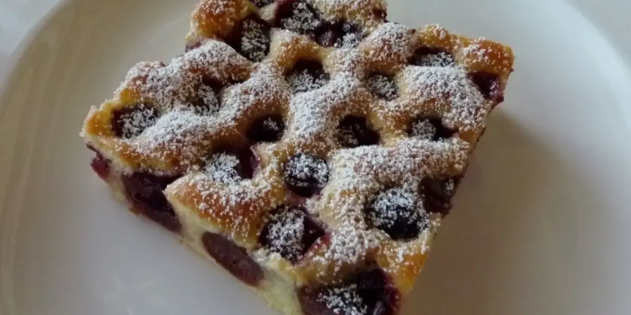Zwei Stücke Kirschstreuselkuchen vom Blech, mit Puderzucker bestäubt, auf einem weißen Teller.