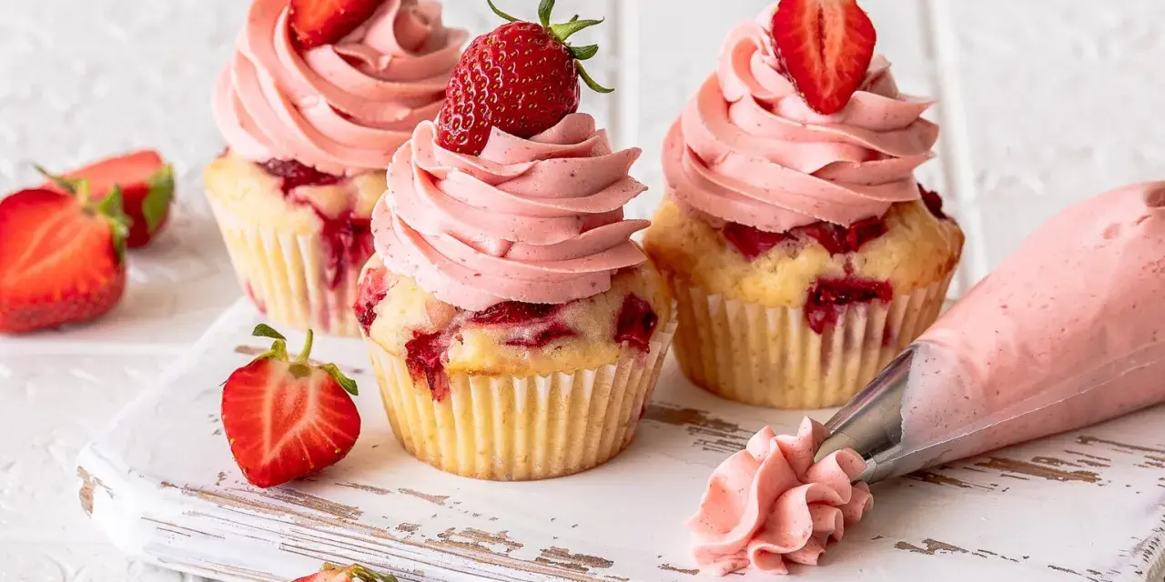 Erdbeer Cupcakes mit rosa Frosting und frischen Erdbeeren. Ein Spritzbeutel zeigt, wie die leckeren Erdbeer Cupcakes entstehen.
