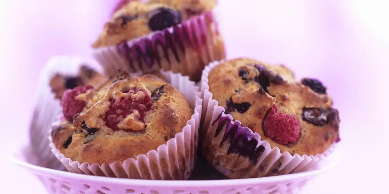 Saftige Muffins mit Obst und Joghurt, garniert mit frischen Himbeeren und Blaubeeren, in einem rosa Körbchen.