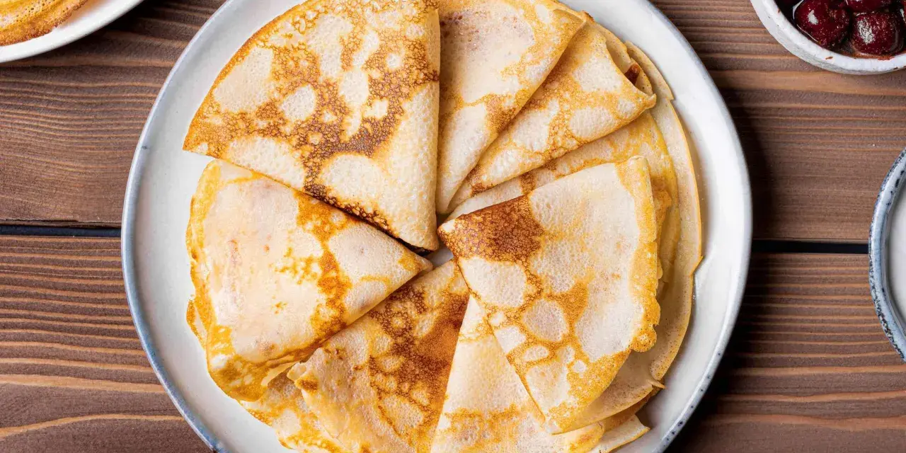 Omas Pfannkuchen-Rezept: goldbraune, gefaltete Pfannkuchen auf einem Teller, daneben eine Schüssel mit Kirschen.