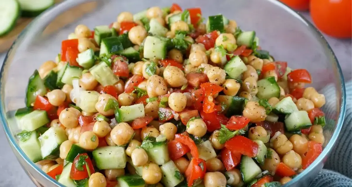 Frischer Kichererbsen Salat mit Gurken, Tomaten und Kräutern in einer Glasschüssel. Ein leichter und gesunder Genuss.